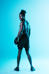 Fototapeta na wymiar serious african american sportsman in boxing gloves looking at camera on blue background