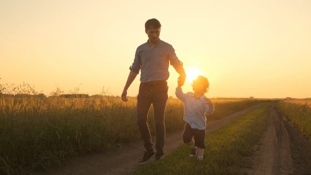Father and son, father and little boy walking on the field at sunset. Go on the road at sunset in a field. 4k Slow motion