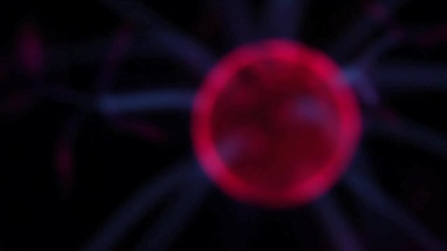 Unfocused plasma ball red center traveling around a pitch black background and with blue rays emitting from it
