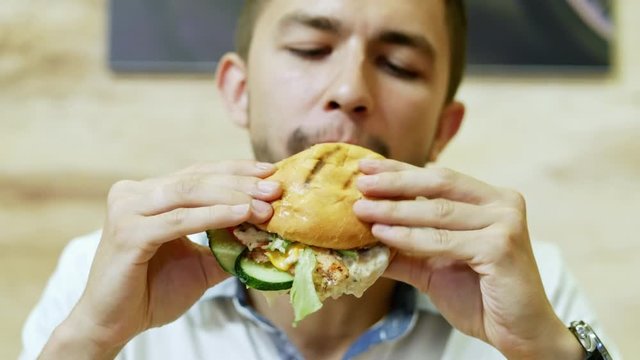 A hungry man eating a juicy burger in a fast food restaurant, delicious food in focus