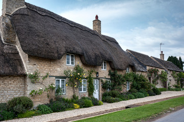 Fototapeta na wymiar Narrow lane with romantic thatched houses and stone cottages in the lovely Minster Lovell village, Cotswolds, Oxfordshire, England 