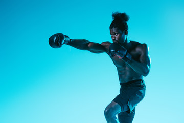 handsome, muscular african american sportsman boxing on blue background
