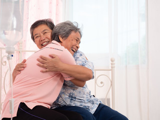 Two asian elderly woman are hugging each other on the bed. Elderly woman patients are happy because...