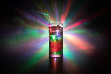 Cocktail glass splashing on dark toned smoky background or colorful cocktail in glass. Party club entertainment. Mixed light.