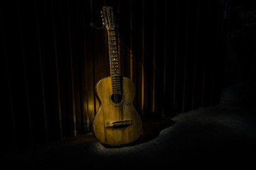 Fototapeta na wymiar An wooden acoustic guitar is against a grunge textured wall. The room is dark with a spotlight for your copyspace.