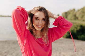 Happy caucasian girl with gentle smile wearing pink clothes posing on summer sandy beach in good sunny day