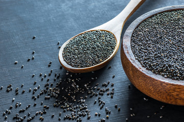 Chia seeds ( Salvia Hispanica ) in wooden spoon and bowl on black wooden rustic background. Cereal...