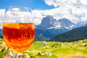 View of the traditional Italian alcoholic drink Aperol Spritz on the background of colorful Italian meadows and the Dolomites Alps mountains. village St. Cristina di Val Gardena Bolzano Seceda, Italy.
