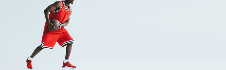 panoramic shot of african american sportsman playing basketball on grey background