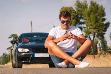 Young man phone poses with his car