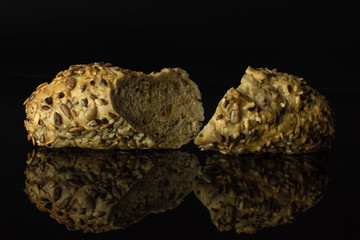 Group of two halves of fresh cereal baguette one sliced isolated on black glass