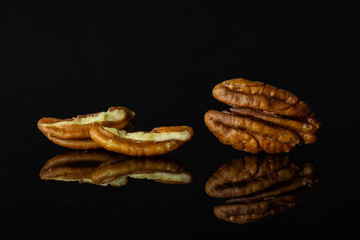 Group of one whole two halves of fresh brown pecan nut half isolated on black glass
