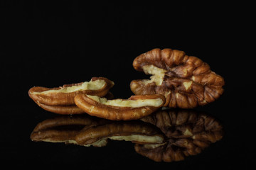 Group of one whole two halves of unshelled fresh brown pecan nut half isolated on black glass