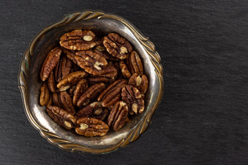 Lot of whole fresh brown pecan nut half in old iron bowl flatlay on grey stone