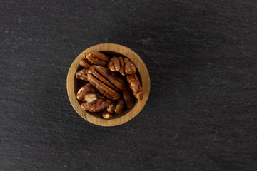 Lot of whole fresh brown pecan nut half copyspace on right in a wooden bowl flatlay on grey stone