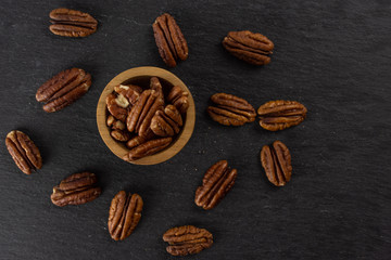 Lot of whole fresh brown pecan nut half in a wooden bowl flatlay on grey stone