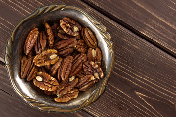 Lot of whole fresh brown pecan nut half in old iron bowl flatlay on brown wood