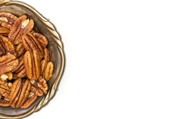 Lot of whole fresh brown pecan nut half copyspace on right in old iron bowl flatlay isolated on white background