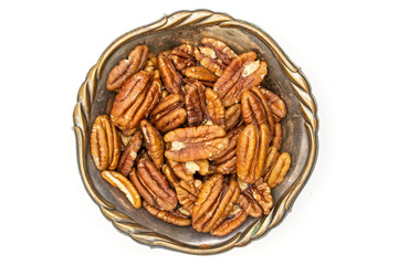 Lot of whole fresh brown pecan nut half in old iron bowl flatlay isolated on white background