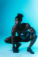 handsome, african american boxer looking away while posing at camera on blue background