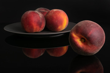 Group of four whole fresh red peach on a gray ceramic plate isolated on black glass