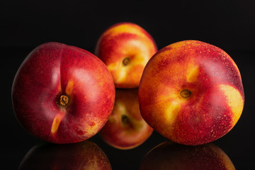 Group of three whole fresh red nectarine two in the front and one in the back isolated on black glass