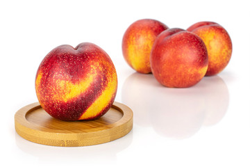 Group of four whole fresh red nectarine on a round bamboo coaster isolated on white background