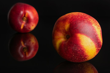 Group of two whole fresh red nectarine one in the front isolated on black glass