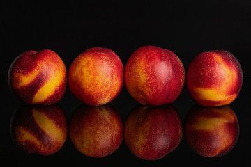 Group of four whole fresh red nectarine in a row isolated on black glass