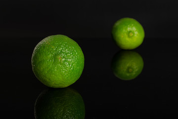 Group of two whole fresh green lime one is in the front isolated on black glass