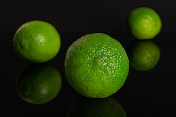 Group of three whole fresh green lime one is in the front isolated on black glass