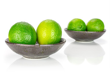 Group of four whole fresh green lime in a dark ceramic bowl isolated on white background