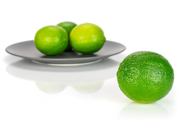 Group of four whole fresh green lime one is in the front and the rest is on a ceramic grey plate isolated on white background