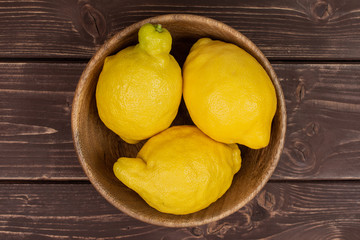Group of three whole fresh yellow lemon in a wooden bowl flatlay on brown wood
