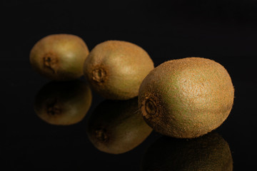 Group of three whole fresh green kiwifruit actinidia deliciosa placed diagonally isolated on black glass