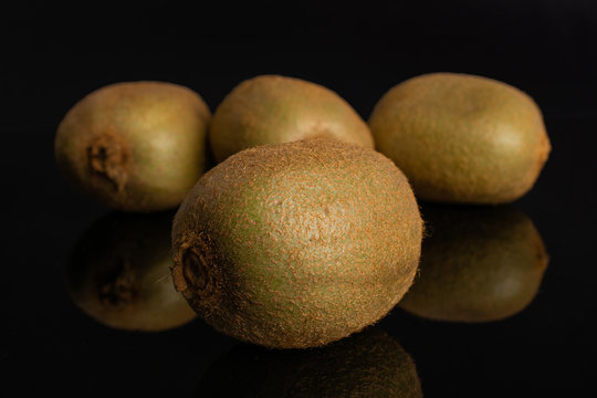 Group of four whole fresh green kiwifruit actinidia deliciosa one is in the front isolated on black glass