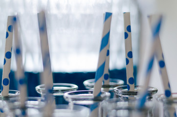 Blue and white striped straws in glass milk bottles with a jug of blue liquid in the background