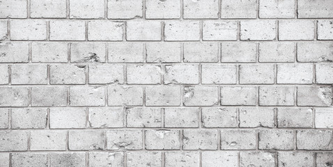 Simple grungy grey white brick wall pattern surface texture wide panorama banner background. Wall weathered under the elements and marked with holes, cracks and imperfections.