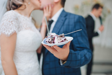 The bride and groom kiss and hold on hand with a plate a delicious wedding cake. Wedding traditions.