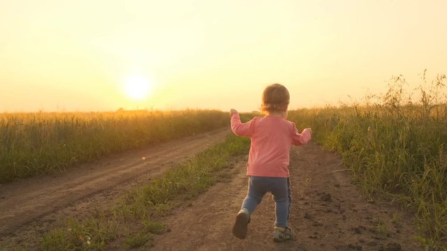 Happy little baby running across the field on a sunset summer day. Slow motion