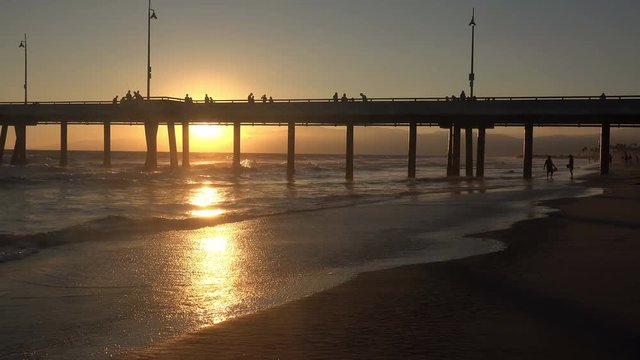 Beautiful sunset behind the Venice Pier with big waves crashing to shore