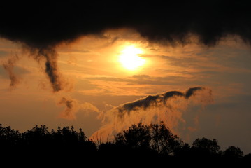 Fototapeta premium Dramatic stormy clouds surrounding sun at sunset over local forest on warm sunny spring day