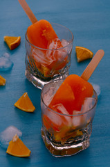 Homemade orange ice cream popsicles on the glass blue background