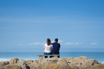 Fototapeta premium Couple sitting on a bench watching the ocean