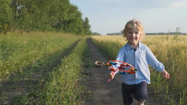 Happy little boy running across the field on a sunset summer day. The boy plays at sunset. runs across the field with a toy. Slow motion