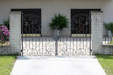 Large wrought iron family house driveway entrance doors mounted on two stone tiles covered concrete...