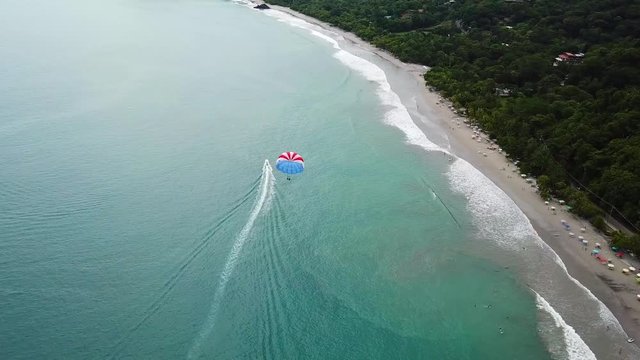 Aerial, tracking, drone shot, panning around a parasail and a boat, on the coast of Manuael Antonio national park, on a cloudy, summer evening, in Jaco, Costa rica