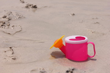 Fototapeta na wymiar Toy watering can on the sand of the sea coast.