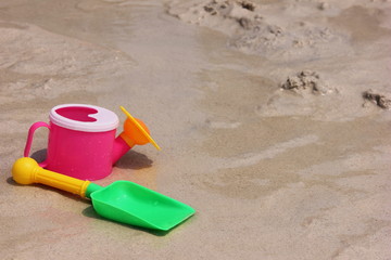 A toy watering can and a toy shovel are located on the sand of the sea coast.
