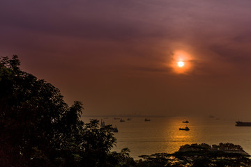 View looking out over the Singapore Strait during sunset with boats, vessels and cargo ships importing and exporting goods on the horizon